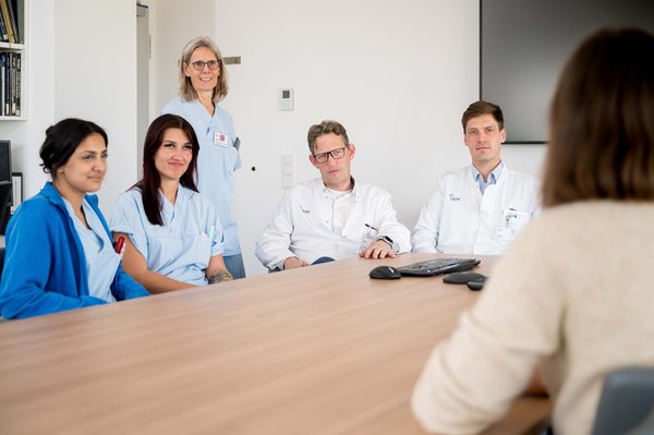 UKM | Presse | Neuroradiologe, Neurochirurg und drei Pflegerinnen mit genesener Patientin an einem Tisch